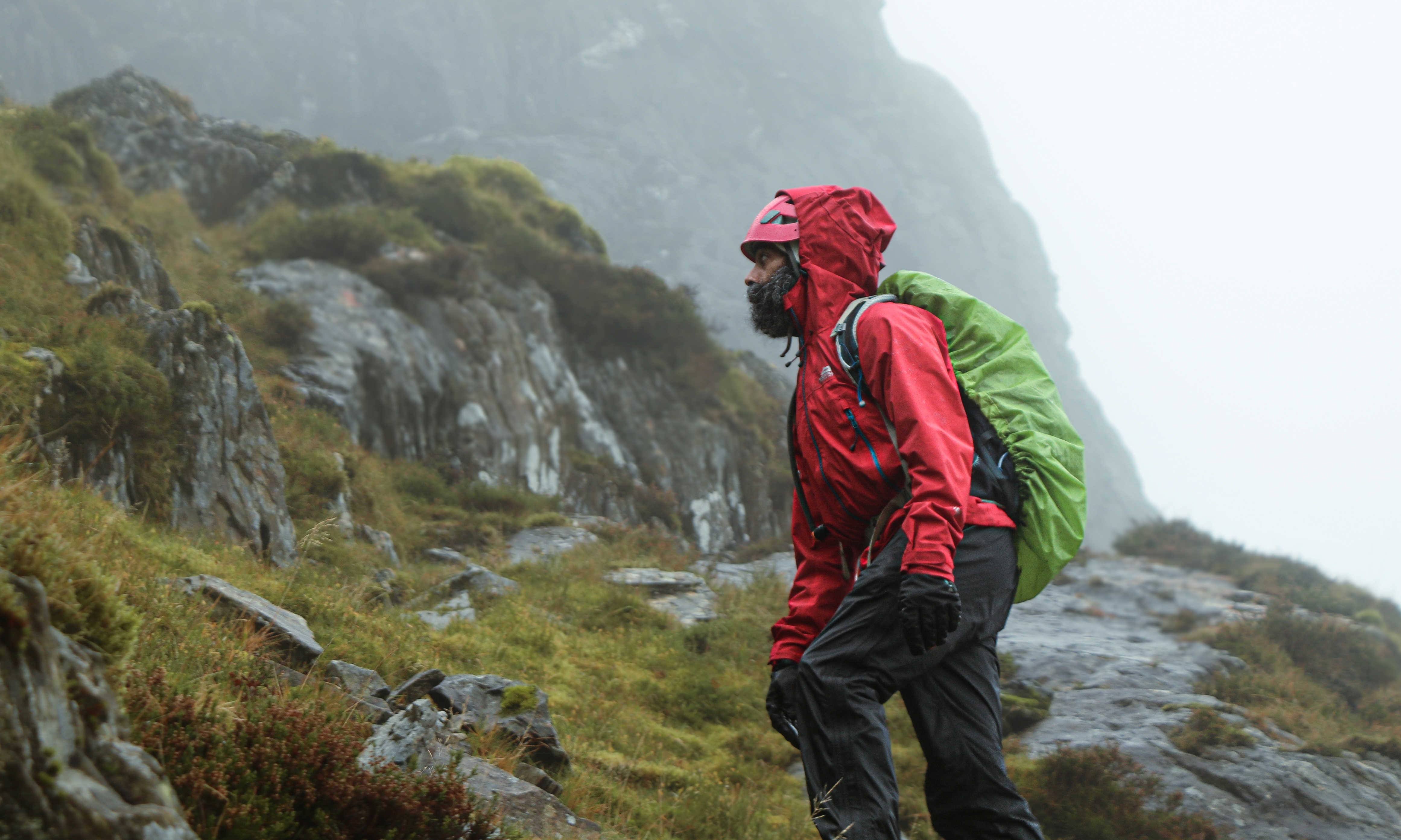 A man of central Asian heritage wearing a helmet and waterproofs prepares to start scrambling