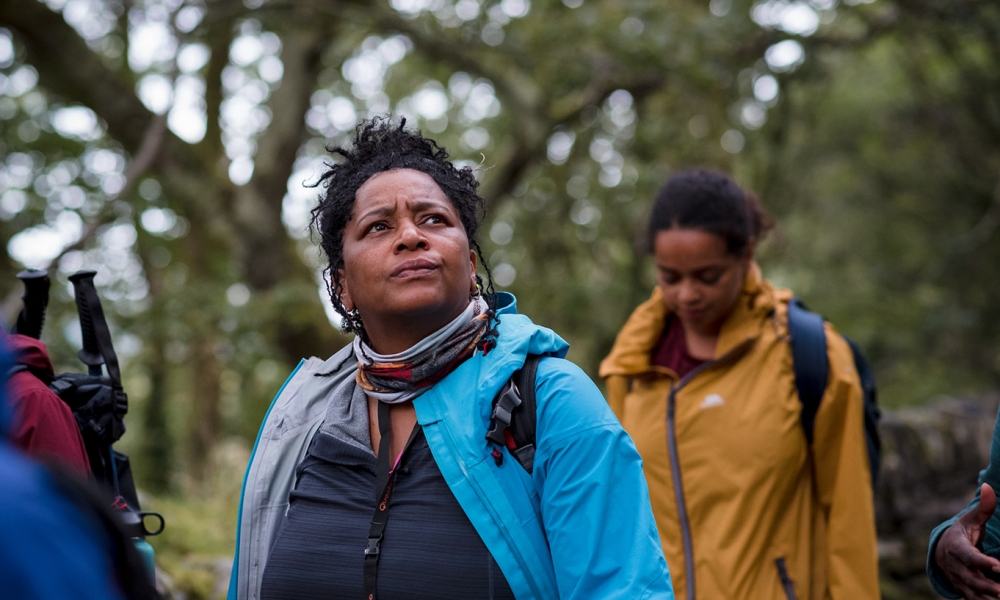 A black hiker looking thoughtful as she walks through lowland terrain with a group