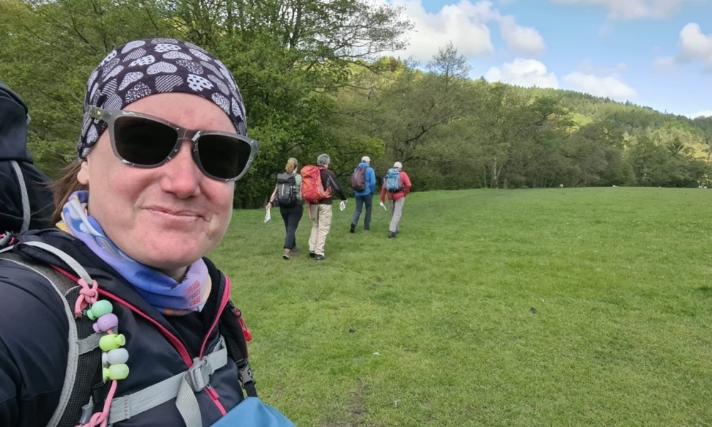 Amy Baron Hall crosses a field bounded by trees with a group of fellow Hill and Moorland Leader trainees.