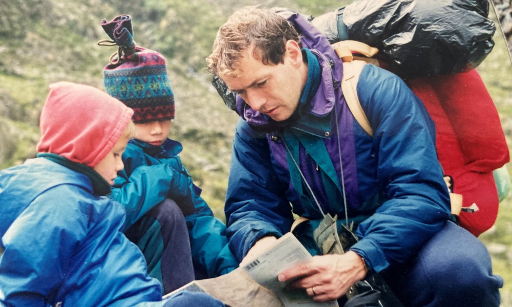 A dad shows his two young children how to use a map. Photo looks to be from the 1980s.